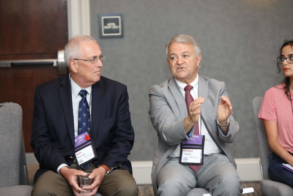 two men, one in black blazer, the other in gray suit, next to a woman in red shirt. Man in middle is explaining something