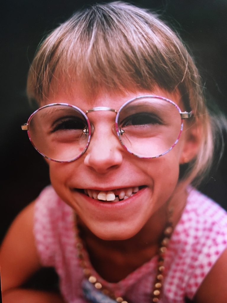 Young blonde girl with VEDS-  giant glasses and crooked teeth smiling