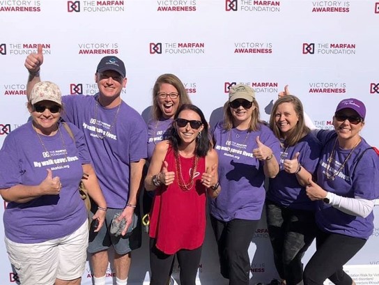 Team VEDS Orlando- Group of people in front of a Marfan Foundation board "thumbs up" and smile!