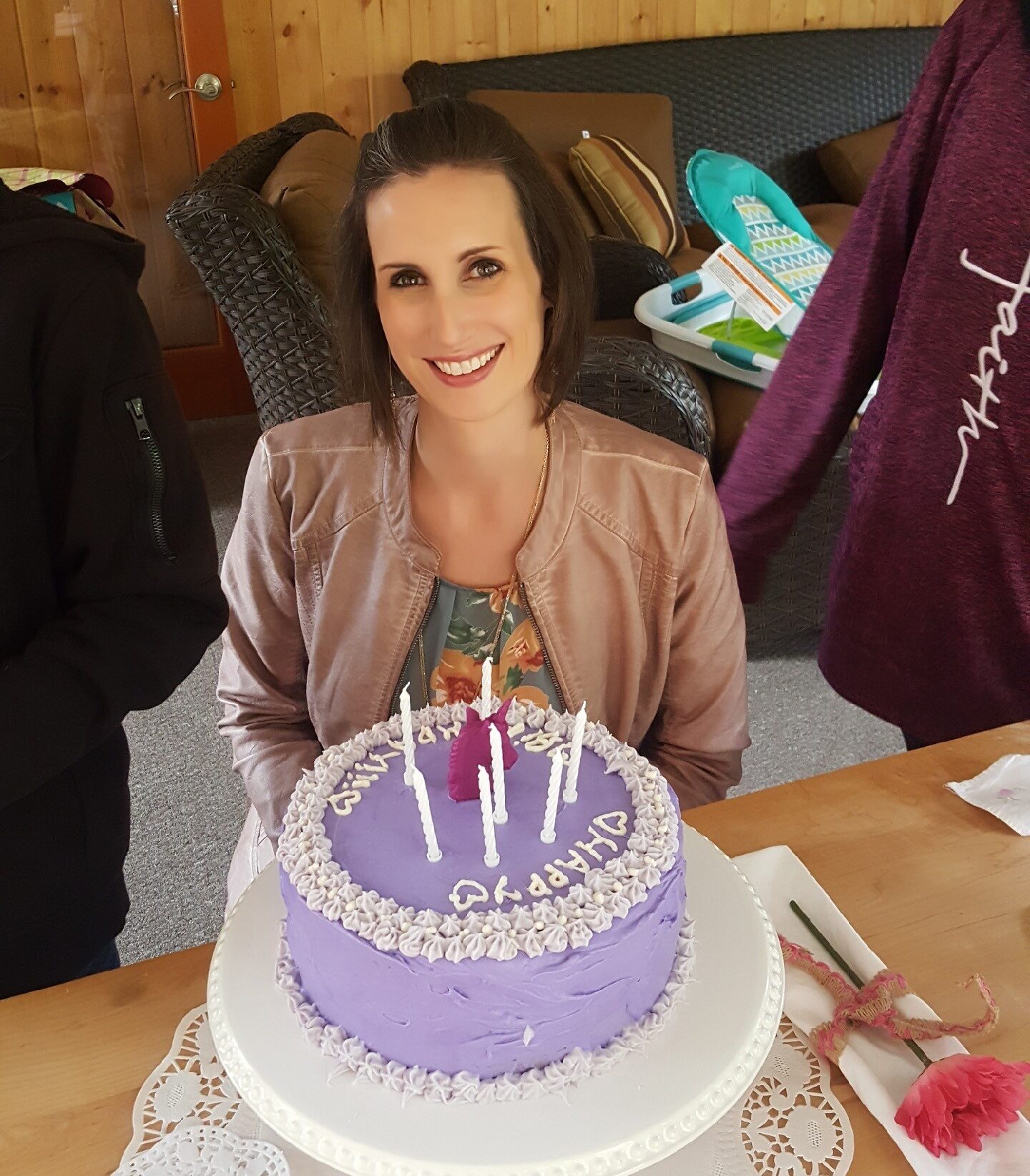 woman with short dark brown hair smiling in front of a purple birthday cake