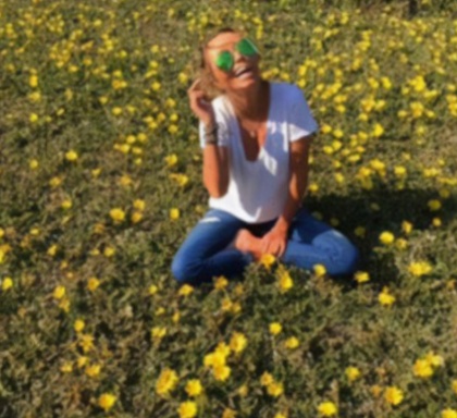 Bella Welch sitting in a field of yellow wildflowers, smiling.